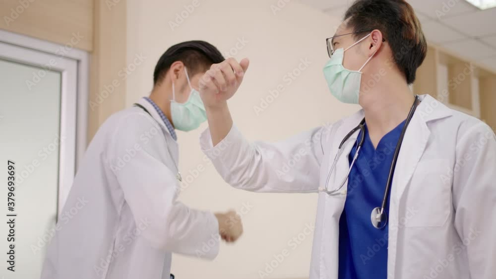 Young two asian doctors greeting together at lobby hallway hospital with elbow bump wearing surgical face mask. New greeting avoid spread of coronavirus in clinic in health care concept Young two asian doctors greeting together at lobby hallway hospital with elbow bump wearing surgical face mask. New greeting avoid spread of coronavirus in clinic in health care concept