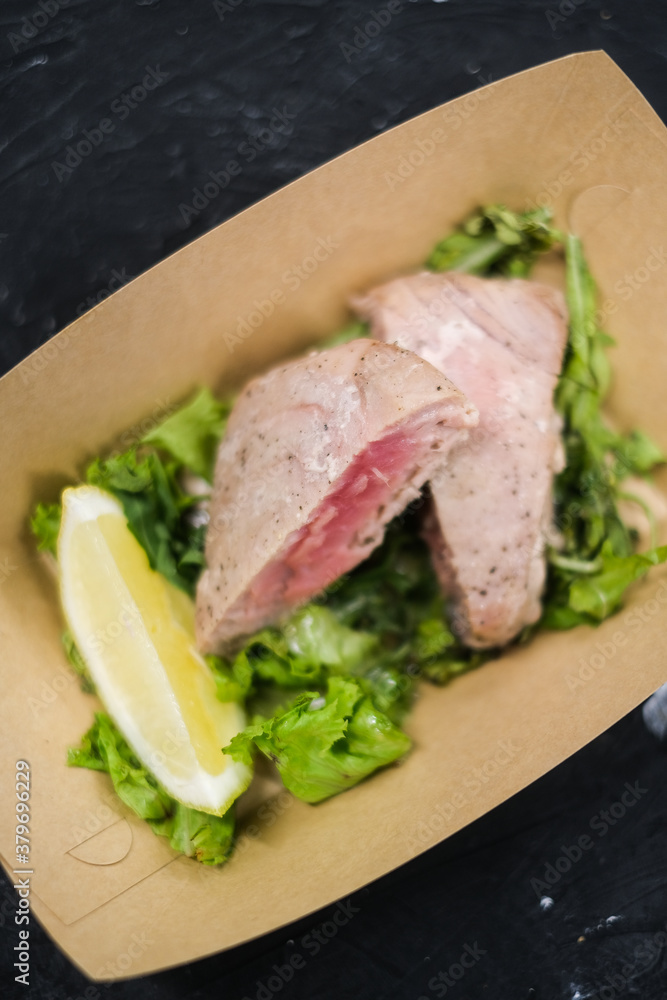 Tuna steak on a salad pillow with a slice of lemon in a paper plate Tuna steak on a salad pillow with a slice of lemon in a paper plate