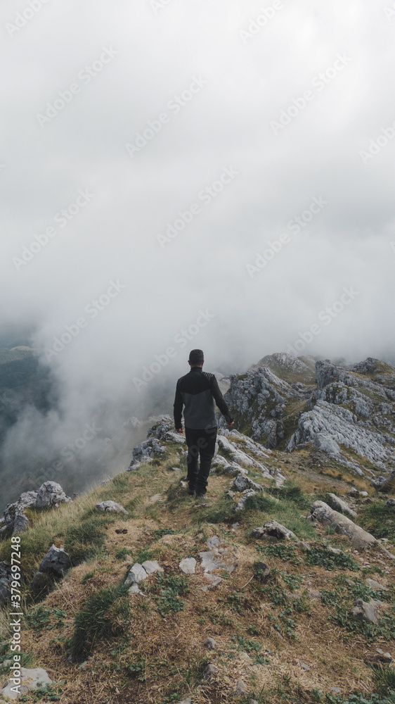 Hombre de espaldas realizando senderismo en las montañas del Parque Natural de Aizkorri-Aratz en el País Vasco en un día de nubes bajas Hombre de espaldas realizando senderismo en las montañas del Parque Natural de Aizkorri-Aratz en el País Vasco en un día de nubes bajas