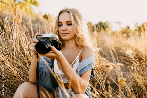 Young woman holding a camera, looking at it, outdoors in a field. © Bostan Natalia