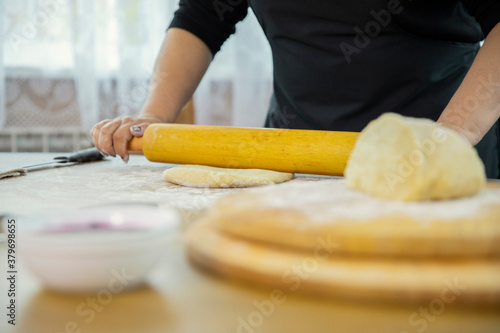 Caucasian housewife rolls out the pizza dough with a rolling pin. Wooden kitchen interior. Festive family dinner. Close-up of hands of a happy housewife.