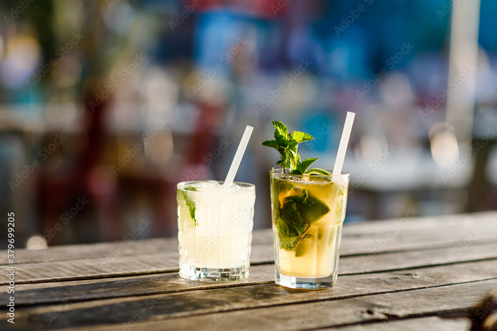 Two glasses fresh alcoholic cooling cocktail in summer on the terrace of a cafe. A refreshing mojito with ice, mint and lime best idea to cool off in the hot summer. Two glasses fresh alcoholic cooling cocktail in summer on the terrace of a cafe. A refreshing mojito with ice, mint and lime best idea to cool off in the hot summer.