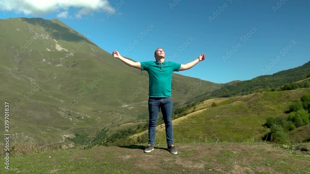 A young man stands in a dress with him arms raised up against the backdrop of mountains. The sun shines brightly from the side of the mountains. Slow motion. A young man stands in a dress with him arms raised up against the backdrop of mountains. The sun shines brightly from the side of the mountains. Slow motion.