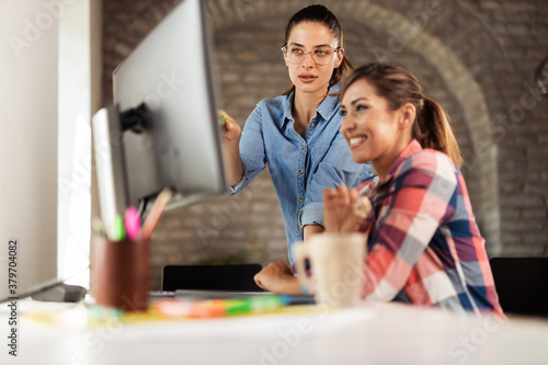 Two young businesswomen cooperating while working on desktop computer in the office