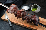 Barbecue dry aged wagyu Brazilian picanha from the sirloin cap of rump beef offered with chimichurri sauce as closeup on a skewer on a wooden design board on rustic black background