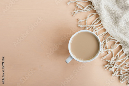 Cup of coffee with pastel beige plaid on wooden background. Autumn or winter composition. Top view  flat lay  copy space