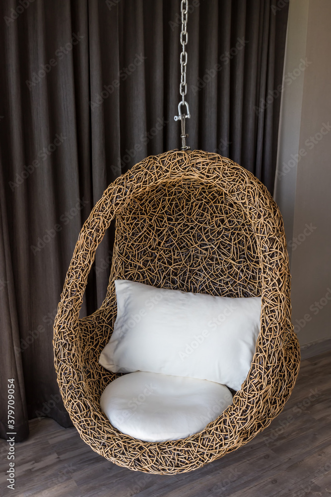 Modern black rattan chair hanging. Hanging chair in room interior. Modern armchair in shape of eggshell