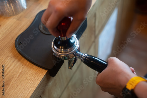Barista pressing coffee in the machine holder. Coffee powder on coffee tamper. barista using tamper to press ground coffee into portafilter to make espresso hot drink.