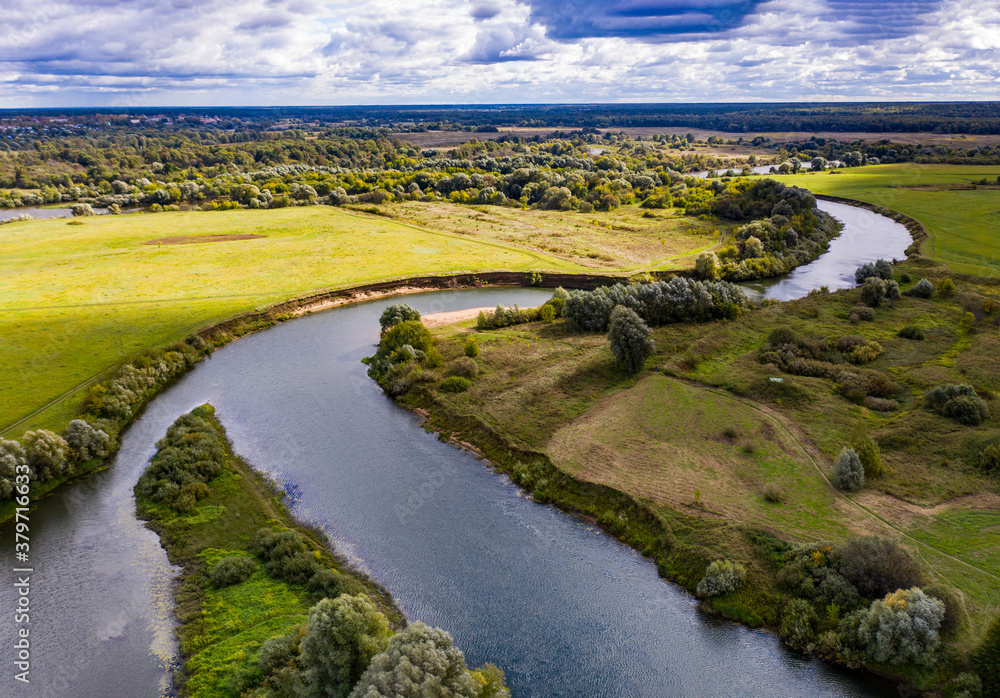 a panoramic view of the white old church on a green meadow between the tributaries of the river against the backdrop of thunderclouds filmed from a drone