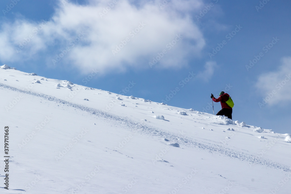 One unrecognizable person climb skiing on a snowy hillside in sunny winter day. Skier hiking to summit of mountain