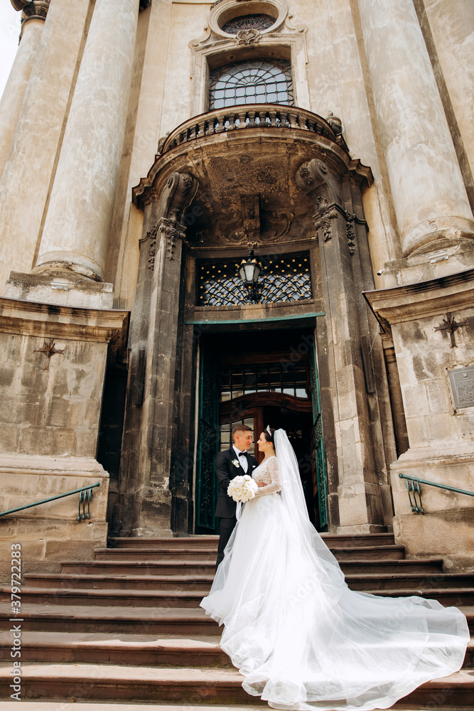 The newlyweds standing on the stairs near the old baroque church