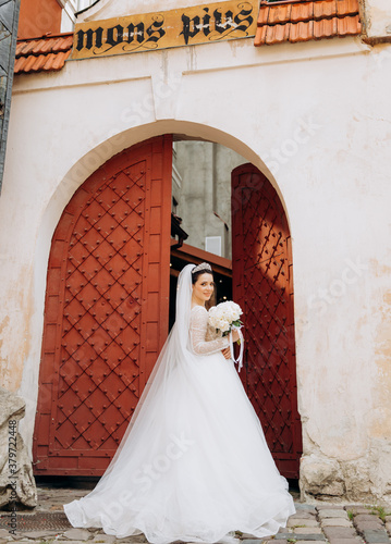 Portrait of a luxury young bride in a white wedding dress with crown on head in the old European city. Woman poses near old door.