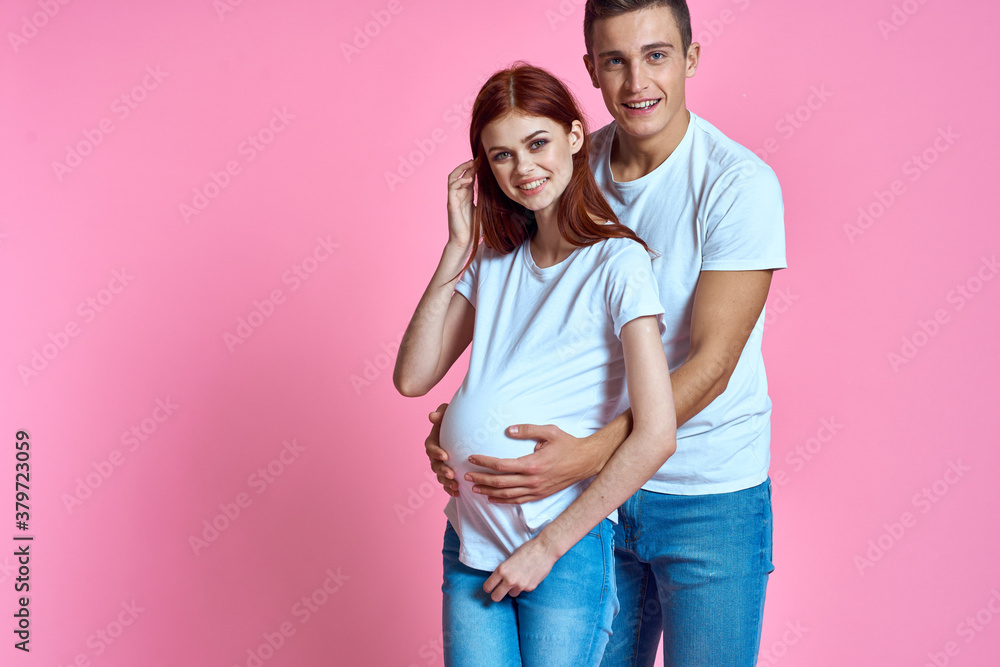 Fototapeta premium pregnant mom and happy father on pink background Young family waiting for baby