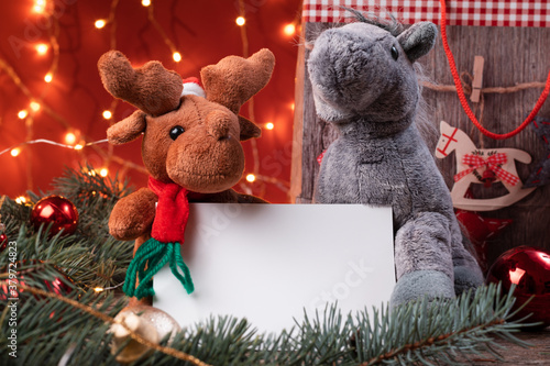 Cute reindeer in santa hat and horse toys holding a white writeable card, sheet of paper in a Christmas scenario. photo