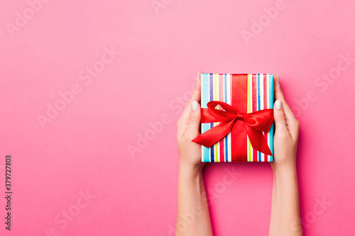 Girl Hands holding craft paper gift box with as a present for Christmas or other holiday on pink background, top view with copy sppace photo