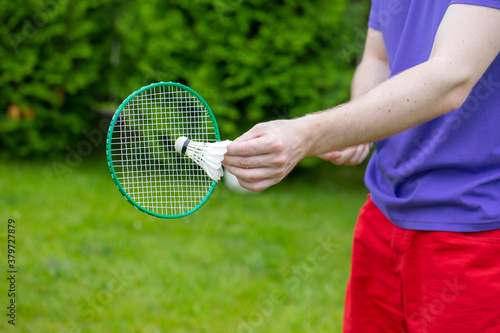 Close up view of young male badminton player holds racket with shuttle on green nature background outdoors. Sport, youth, activity, power concept. Resting time. Summer, leisure, hobby