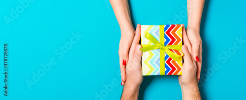 Top view of giving and receiving a gift on colorful background. Present in male and female hands. Love concept. Close up