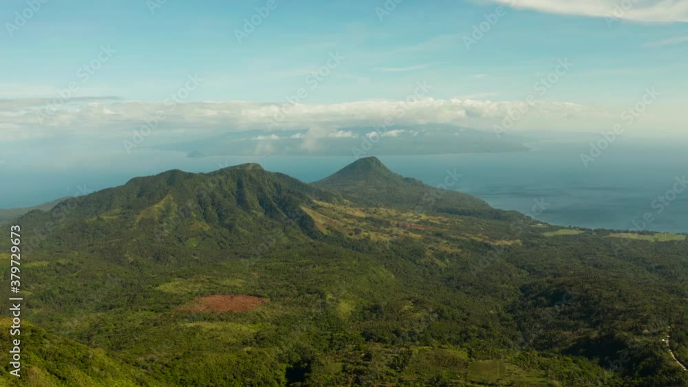 Mountains covered rainforest, trees and against blue sea with blue sky with clouds, aerial view. Camiguin, Philippines. tropical landscape. Mountain landscape on tropical island with mountain peaks Mountains covered rainforest, trees and against blue sea with blue sky with clouds, aerial view. Camiguin, Philippines. tropical landscape. Mountain landscape on tropical island with mountain peaks