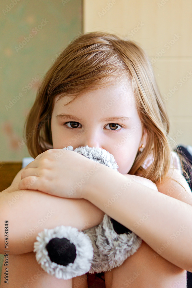 Dramatic portrait of little girl sitting on chair and cuddling teddy bear with sad face. Unhappy child sitting alone and looking out with worrying face. Dramatic portrait of little girl sitting on chair and cuddling teddy bear with sad face. Unhappy child sitting alone and looking out with worrying face.