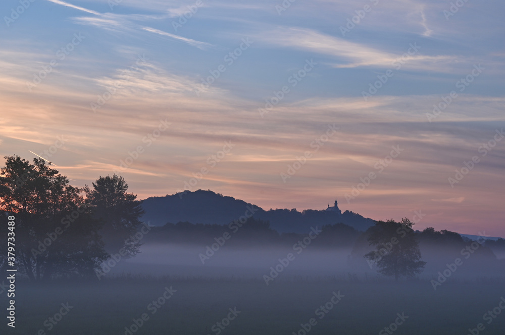 Morgenstimmung vor Sonnenaufgang und Nebel im Tal mit Hügel im Hintergrund