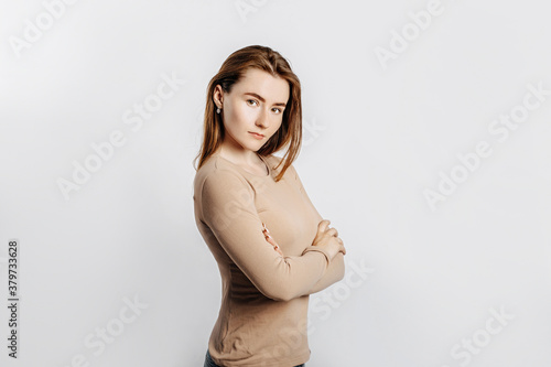 Beautiful young girl smiling and posing looking at the camera on a white isolated background. Positive brunette woman in a beige jumper. Kind look.