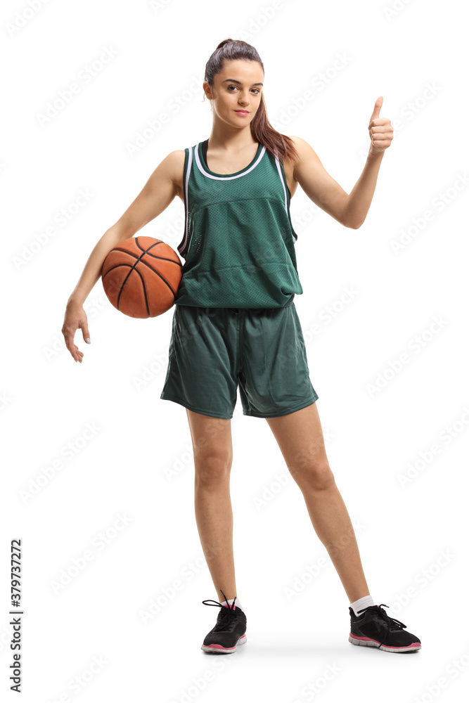 Full length portrait of a female basketball player with a ball under arm showing thumbs up