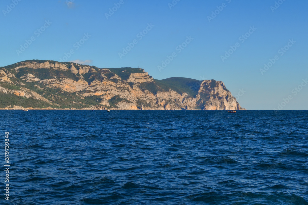 red orange stone rock mountain stands on shore of the blue sea on a bright sunny day, summer sky with clouds