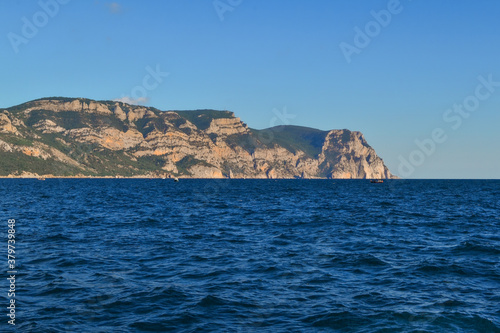 red orange stone rock mountain stands on shore of the blue sea on a bright sunny day, summer sky with clouds