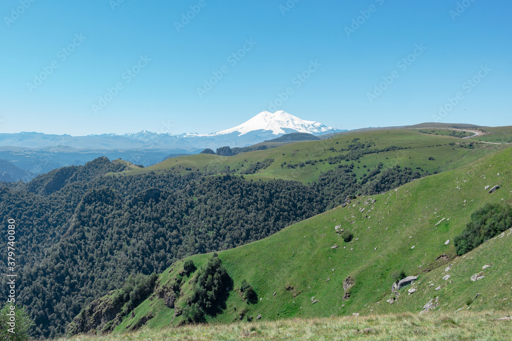 Fototapeta premium Scenic view of the highest peak in Europe, mount Elbrus with green hills on a Sunny summer day.