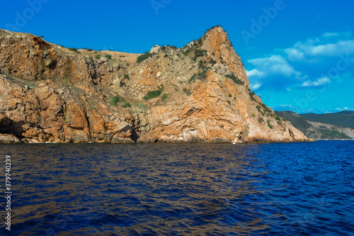 red stone rock stands on shore of the blue sea on a bright sunny day, summer sky with clouds