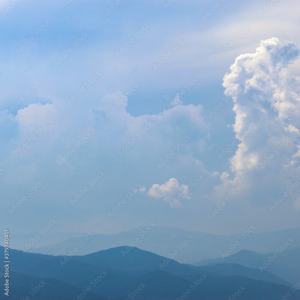 Mountains and hills in the distance. Blue silhouette of a mountain in the distance, with clouds in the blue sky. Mountains and hills in the distance. Blue silhouette of a mountain in the distance, with clouds in the blue sky.