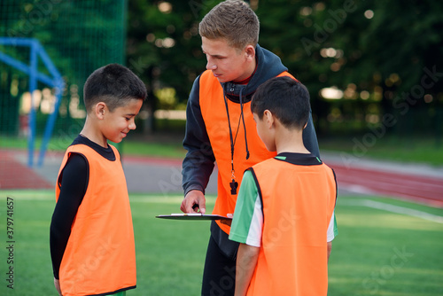 Football coach instruct teen football players. Young professional coach explains for kids the strategy of the game.