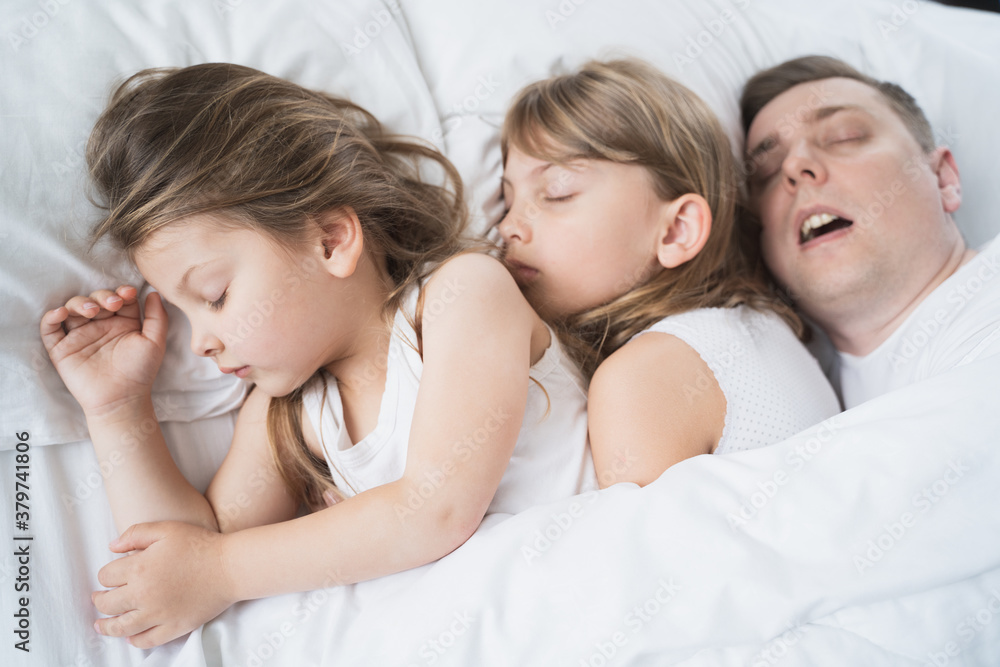 Kids, daughters, dad sleep together in bed on pillows under blanket. Father is snoring hard. Family joint sleeping. Insomnia, night bedtime.Sweet dreams. arly wake up,rise to kindergarten,school,work Kids, daughters, dad sleep together in bed on pillows under blanket. Father is snoring hard. Family joint sleeping. Insomnia, night bedtime.Sweet dreams. arly wake up,rise to kindergarten,school,work