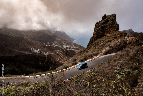 A car driving down this mountain road with a beautiful view of a small town in the hillside.