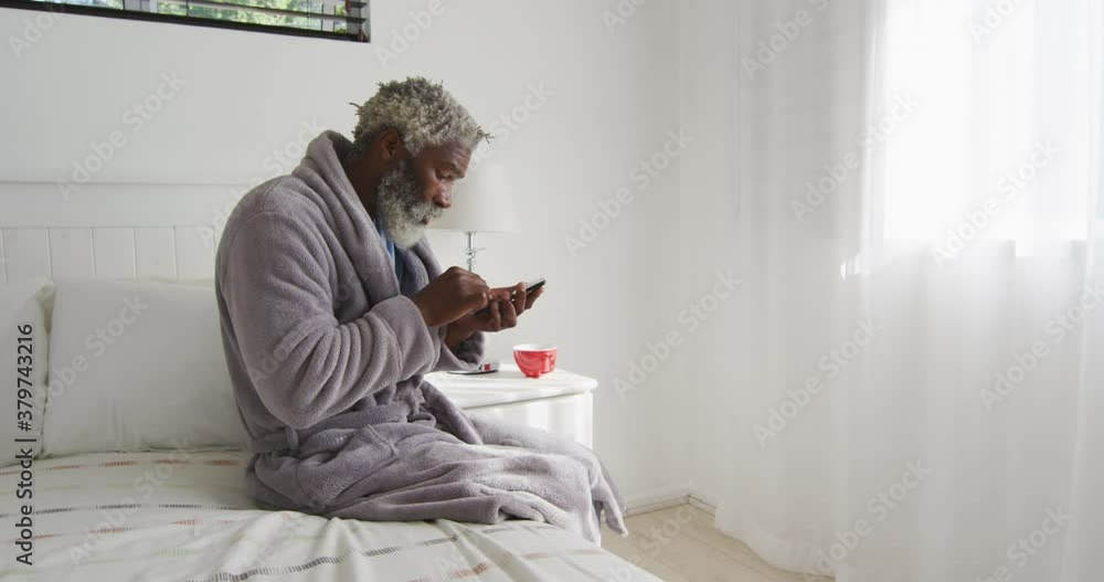 Senior man using smartphone while sitting on bed at home Senior man using smartphone while sitting on bed at home