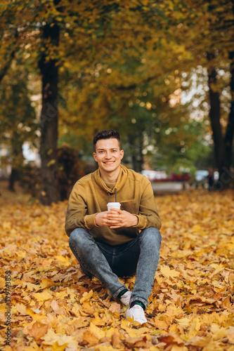 Portrait of handsome and happy boy smiling and drinking coffee in the autumn park