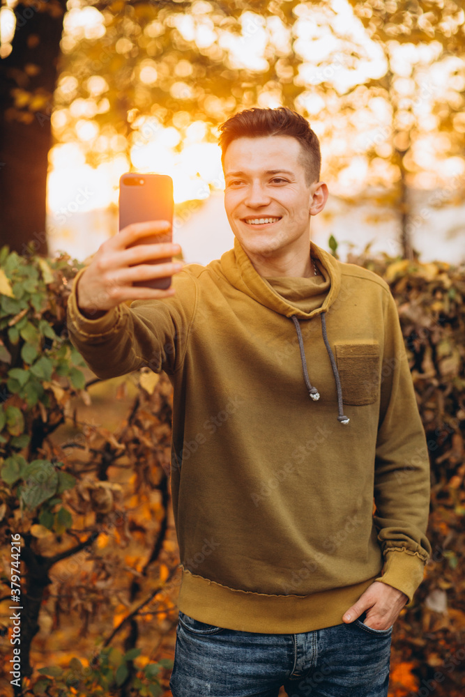 Portrait of handsome and happy guy smiling and holding a bouquet of autumn leaves and taking a selfie in the park Portrait of handsome and happy guy smiling and holding a bouquet of autumn leaves and taking a selfie in the park