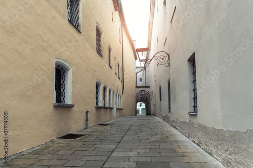 Narrow inner paved stone urban street road passage in old european city. Vintage dark alley with lamp lantern and grey wall. Nobody scenic town view © Kirill Gorlov