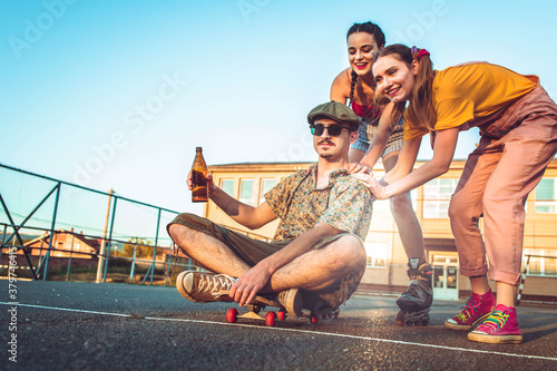 Friends hanging out. Two girls push their male friend on the skate board © stivog