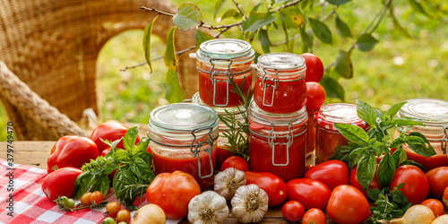 Homemade tomato preserves in glass jars and fresh tomatoes and herbs on a wooden table in the garden photo