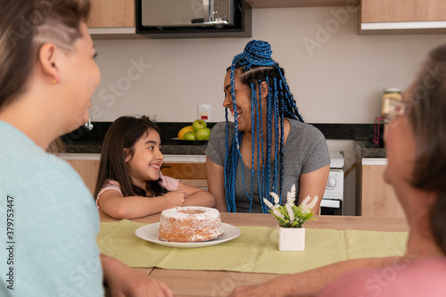 Joyful latin lesbian homosexual couple with big smile relaxing and enjoying at kitchen table, inside. Family, affectionate, same sex family, together concept.. photo