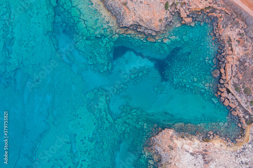 An aerial view of the beautiful Mediterranean Sea, where you can see the cracked rocky textured underwater corals and the clean turquoise water of Protaras, Cyprus,