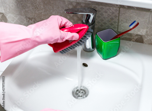 Woman hands in pink rubber gloves cleaning washing sink in bathroom. Close up. Disinfection of bath. 