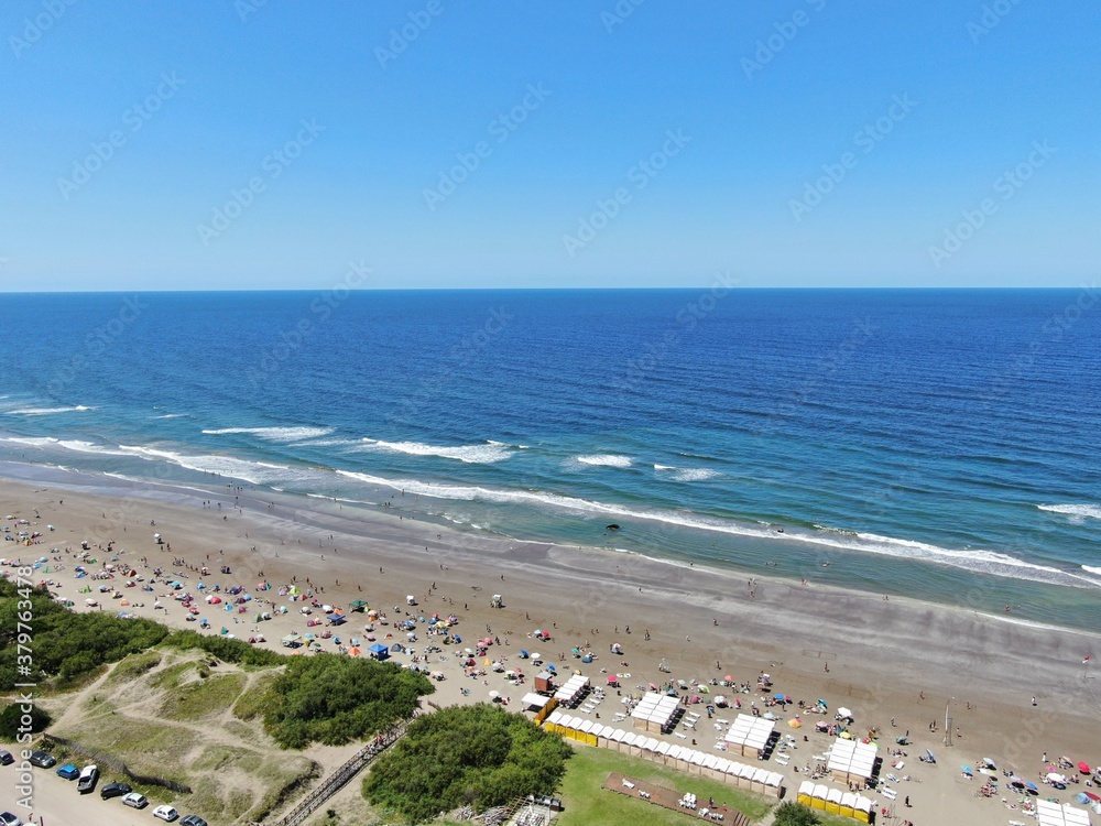 Vista aérea de una zona de playa con gente en la playa y al fondo el mar azul , durante un día soleado de verano.