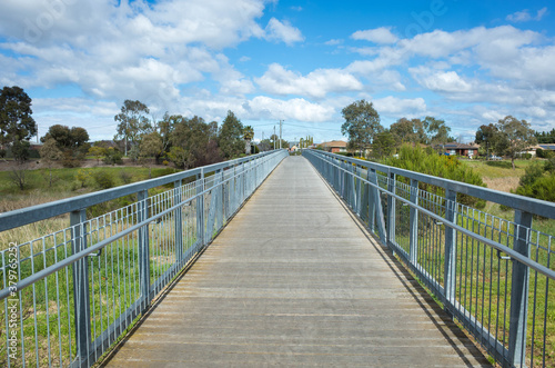 A pedestrian footbridge/boardwalk over wetlands leads to an Australian neighbourhood with some residential houses in the distance. Skeleton Waterholes Creek, Melbourne, VIC Australia. © Doublelee