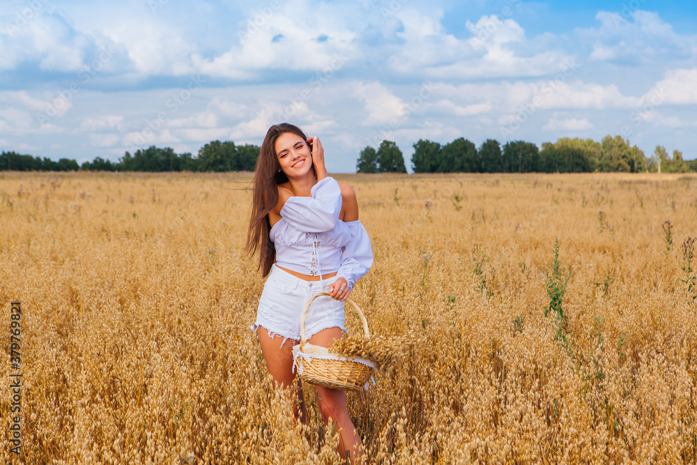 Young beautiful woman at golden oat field holding basket with ears of oats.