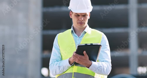 Professional architecture inspector working with digital tablet at construction site, tracking shot photo