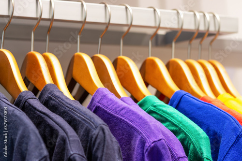 Multicolored T-shirts hang on wooden hangers in the store, side view