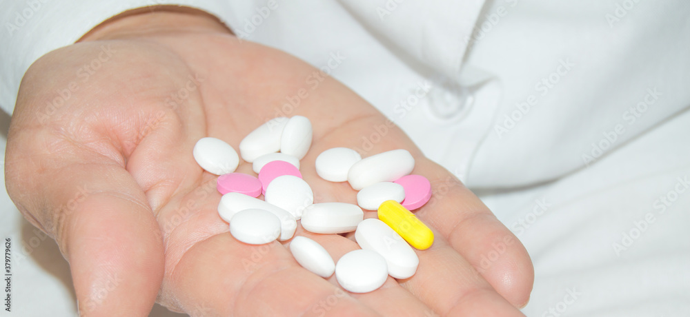 Open palm of a woman with a bunch of white and pink pills, health and medicine concept, close-up