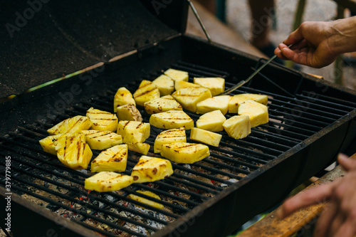 Man Tending To Sliced Pineapple Cooking Over BBQ Grill photo